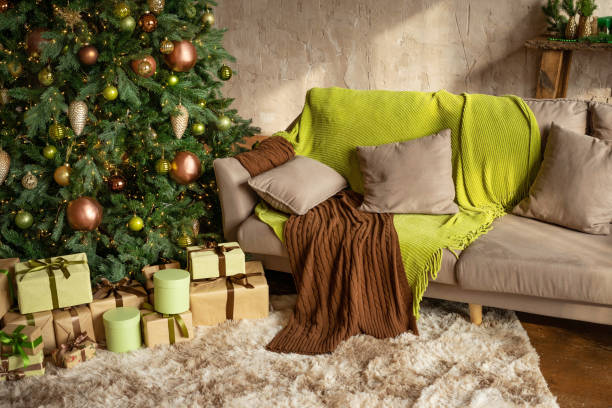 istock Modern Christmas living room interior in studio apartment. Large decorated Christmas tree, sofa, plaid, gift boxes, fluffy carpet, light garlands. Trending colors 2022: green, coffee, beige, khaki. 1407021614