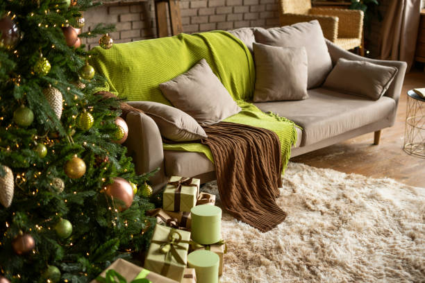 istock Modern Christmas living room interior in studio apartment. Large decorated Christmas tree, sofa, plaid, gift boxes, fluffy carpet, light garlands. Trending colors 2022: green, coffee, beige, khaki. 1407021630