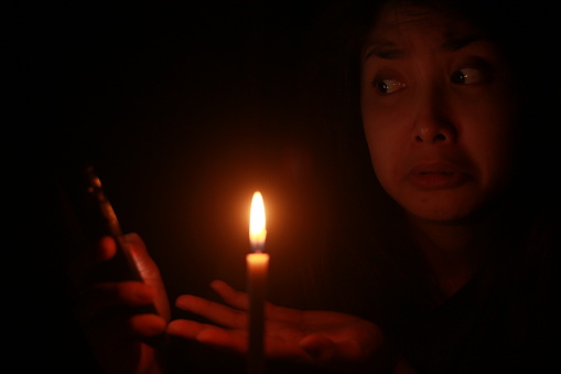 an Asian woman shocking pointing cellphone in front of candle light in the dark night