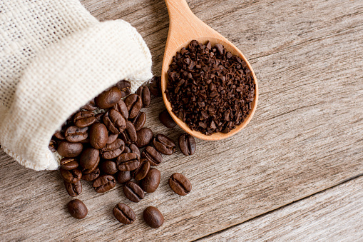 Roasted coffee bean in hemp sack and granuleatd coffe in scoop on  wood table background. Top view. Flat lay.