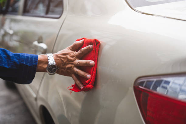 istock Man's hand cleaning car & drying vehicle with microfiber cloth. Hand wipe down paint surface of shiny blue sedan after polishing and ceramic coating. Car detailing, maintenance, and car wash concept. 1407035428