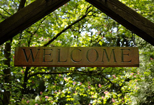 Wooden welcome sign hanging in front of green trees