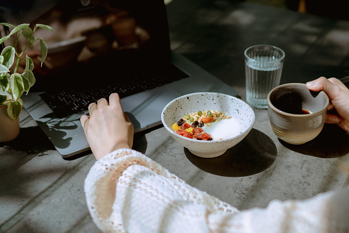 Young businesswoman having works remotely from the comfort of her home during his breakfast.