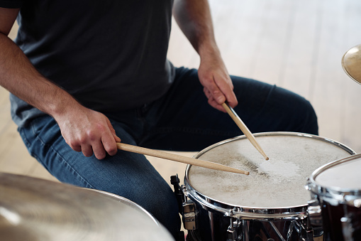Close-up of young drummer beating with drumsticks on drums during playing song