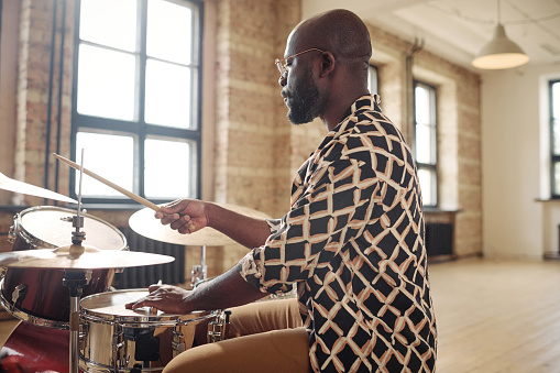 Young African drummer playing at drums set during rehearsal at musical studio