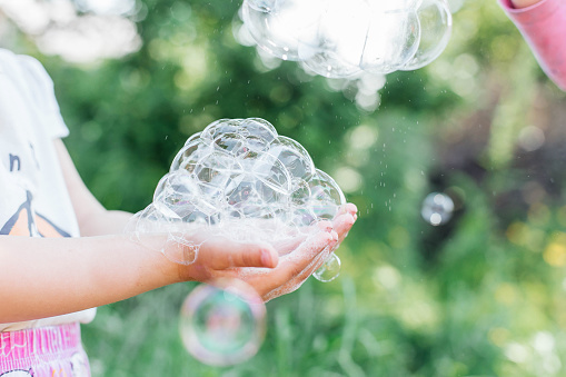 Little Girl holding soap bubbles in her hands. Children play with soap bubbles in nature. Summer holidays, summer games in nature.