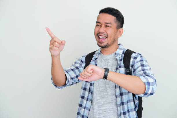 istock Adult Asian man wearing backpack pointing forward with happy expression while showing his watch 1407042740