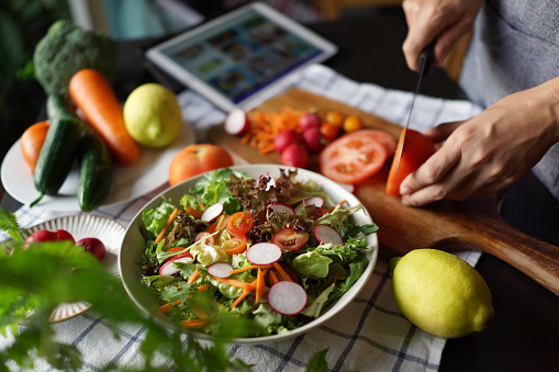 Woman reading a recipe on a digital tablet while preparing salad bowl
