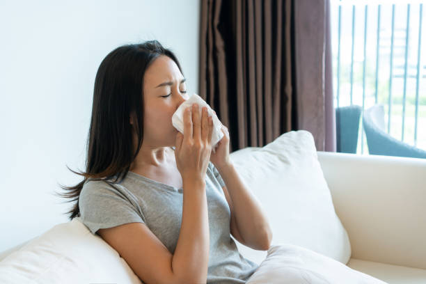 sick young asian woman sitting on couch blowing her nose on a tissue conceptual of healthcare , seasonal flu, rhinitis or an allergic reaction in hay fever. closeup - hay fever imagens e fotografias de stock