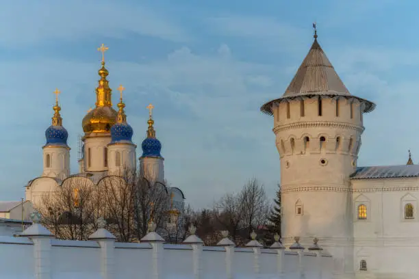 Old tower with a wooden roof and the golden-domed domes of the white-stone St. Sophia Cathedral of the ancient Kremlin in Tobolsk (Russia) in the golden rays of the morning sun. Blue sky with clouds