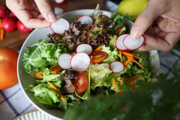 istock Female Hand putting fresh red radish into a bowl with different vegetables 1407047533