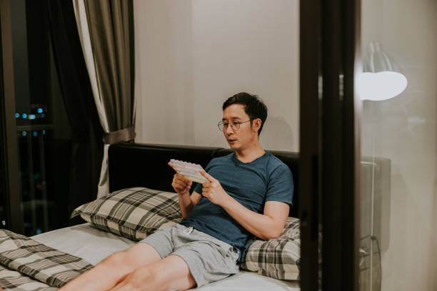 азиатский мужчина смотрит на свою аптечку, чтобы снова проверить и пересчитать лекарство перед сном. - again been green healthy lifestyle стоковые фото и изображения