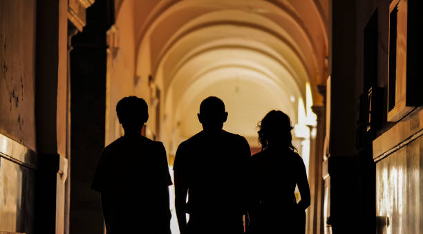 Silhouette of three people on building corridor with sunlight and shadow