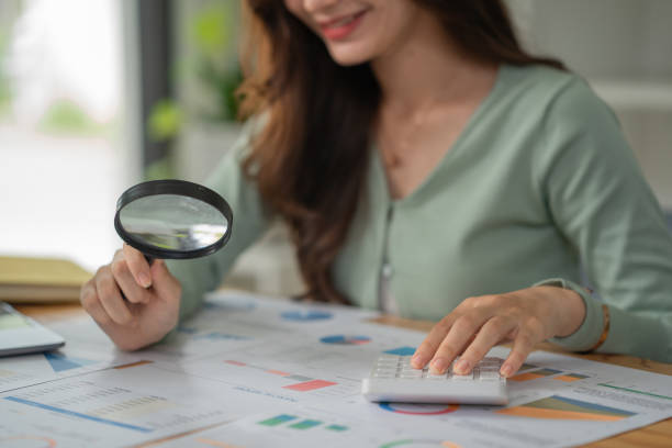 a woman uses a magnifying glass to look at the numbers in the report and uses a calculator to calculate. - condition text magnifying glass contract imagens e fotografias de stock