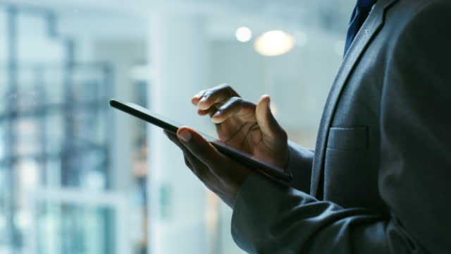 Closeup of one businessman in suit using a digital tablet device in an office. Hands on entrepreneur and dedicated manager searching internet, working online with a touch screen