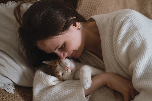 young woman holding cute ginger cat with green eyes. Female hugging her cute short hair kitty in bedroom. Copy space, close up. Adorable domestic pet concept.