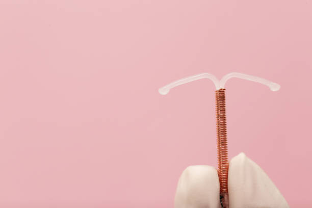 médico sosteniendo un dispositivo anticonceptivo intrauterino en forma de t sobre fondo rosa, primer plano. espacio para texto - iucds fotografías e imágenes de stock