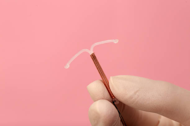 Doctor holding T-shaped intrauterine birth control device on pink background, closeup Doctor holding T-shaped intrauterine birth control device on pink background, closeup diaphragm contraceptive stock pictures, royalty-free photos & images