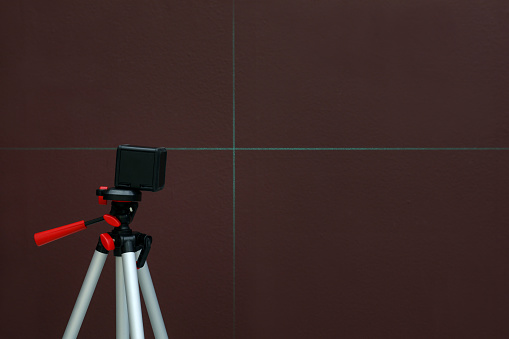 Cross line laser level on tripod in front of brown wall