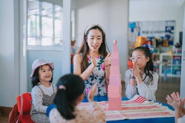 asian Chinese Montessori preschool teacher and students clapping hands successfully complete building tower with toy block in classroom asian Chinese Montessori preschool teacher and students clapping hands successfully complete building tower with toy block in classroom teachers stock pictures, royalty-free photos & images