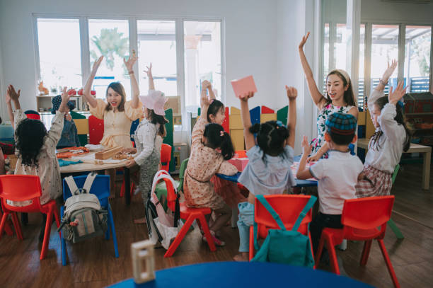 Asian Montessori preschool student raised hands in the class answering question stock photo