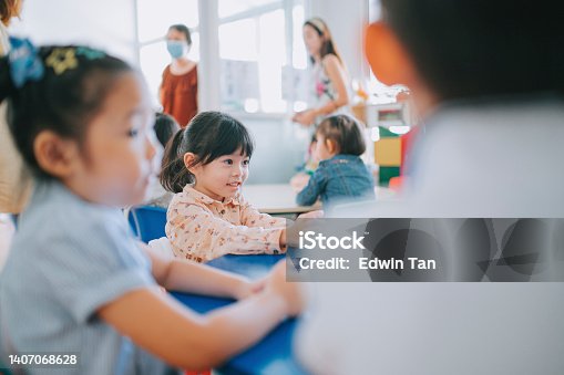 istock excited asian chinese Montessori preschool girl sitting in classroom with her classmate first day of school 1407068628