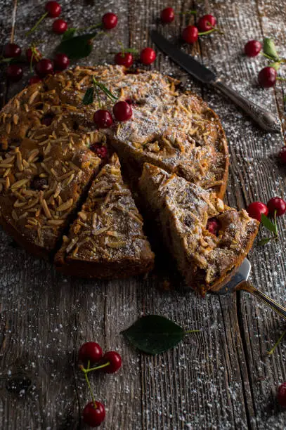 Rustic whole wheat cake with sour cherries and almond topping. Served isolated on wooden table background. Vertical image with copy space