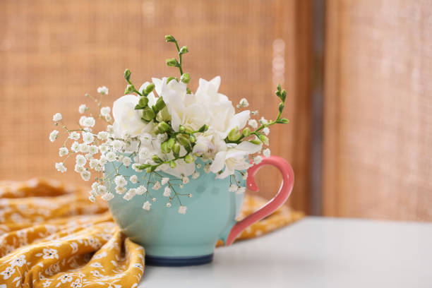 屋内の白いテーブルの上にカップと布地の美しい明るい花。テキスト用のスペース