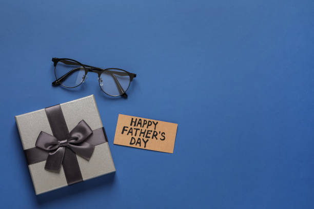 istock Card with phrase HAPPY FATHER'S DAY, eyeglasses and gift box on blue background, flat lay. Space for text 1407071614