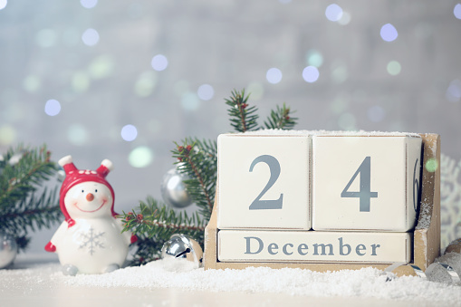 December 24 - Christmas Eve. Wooden block calendar and festive decor on snow against blurred lights