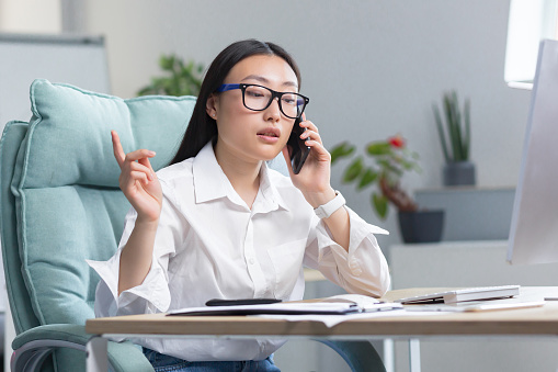 Successful business woman working in modern office, Asian woman talking on the phone, female worker wearing white shirt.