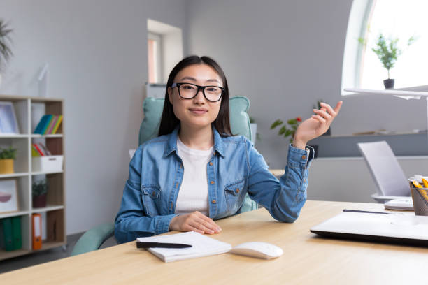 jeune belle femme asiatique parlant sur appel vidéo, femme d’affaires travaillant dans un bureau moderne, souriant et regardant la caméra web, conférence en ligne - working smiling equipment car photos et images de collection