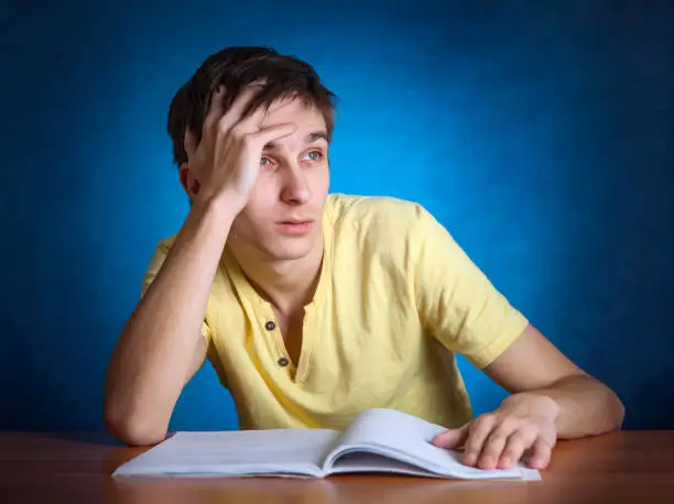 Sad and Stressed Student at the School Desk on the Blue Background