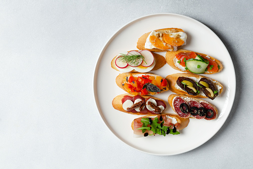 Brushetta, antipasti  or authentic traditional spanish tapas set on white plate. Variety of  pinchos (pintxos) in a bar or restaurant or home party or picnic. Flat lay, top view, copy space for text