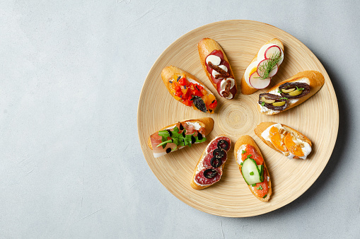 Brushetta, antipasti  or authentic traditional spanish tapas set on wood plate. Variety of  pinchos (pintxos) in a bar or restaurant or home party or picnic. Flat lay, top view, copy space for text