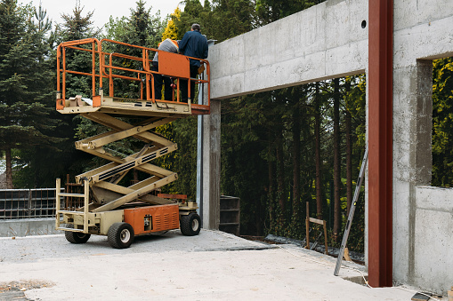 Plataforma elevadora de tijera con trabajadores en un sitio de construcción cerca de la pared photo