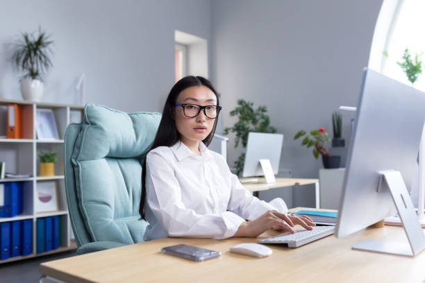 portrait d’une employée de bureau asiatique à succès, regardant l’appareil photo souriant, femme d’affaires en lunettes travaillant et tapant sur un ordinateur - working smiling equipment car photos et images de collection