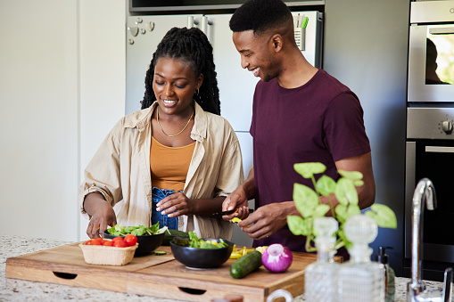Smiling young African couple chopping vegetables for a healthy lunch while standing together at a kitchen island at home