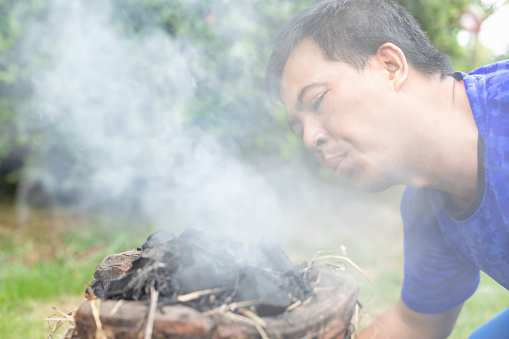 Man blowing to  the stove for setting fire for cooking at outdoor. Smoke on face while blowing
