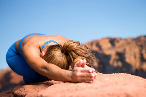 Brazilian Woman with blue outfit practicing yoga kneeling in red rock canyon Vegas.