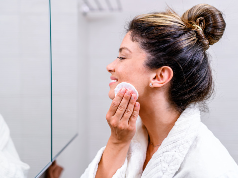 Portrait of a beautiful woman in a bathrobe looking herself in the mirror and cleaning her face.