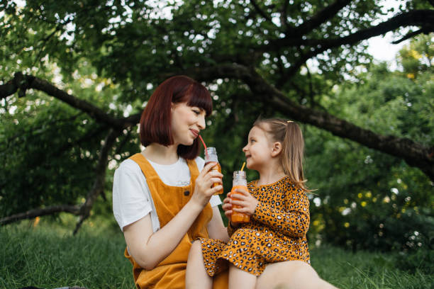 nahaufnahmeporträt einer alleinerziehenden mutter mit kleiner tochter, die mit dem trinken von saft beschäftigt ist - child little girls single flower flower stock-fotos und bilder