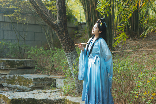 Chinese beauty in Hanfu is holding a flute by the lake
