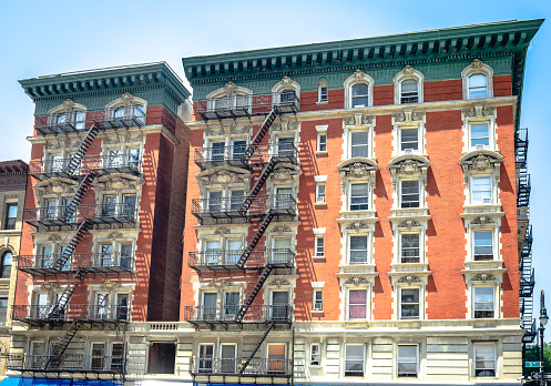 New York, USA -  July 12 2014: The facade of a red brick residential building on the corner of 5th Ave and W 120 st, with black metal emergency stairs.