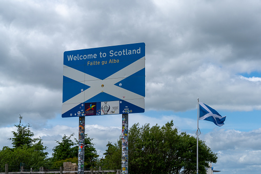 Jedburgh, United Kingdom - 18 June, 2022: Scottish flag and Welcome to Scotland sign in English and Scots at a rest stop at the Scottish Borders