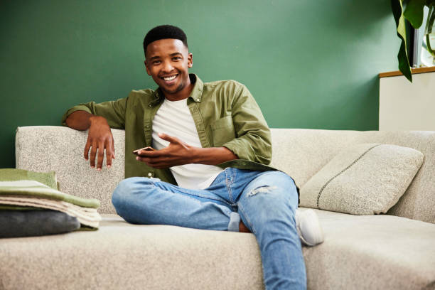 istock Smiling young man sitting on a sofa with a mobile phone 1407081537