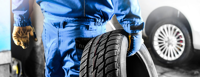 Mechanic holding tire with copy space for text repair service center, blurred background, Maintenance transport  panorama or banner photo.