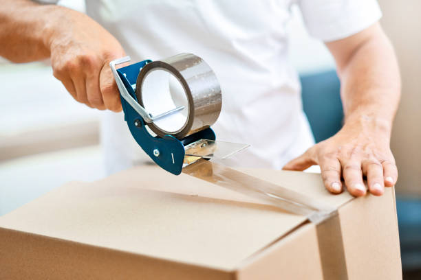 istock Worker hands holding packing machine and sealing cardboard or paper boxes 1407081768