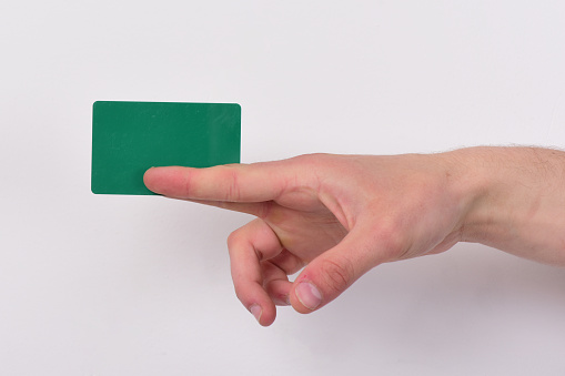 Hand isolated on light grey background. Advertising and introducing concept. Male hand holds dark green card. Piece of paper in close up and copy space.