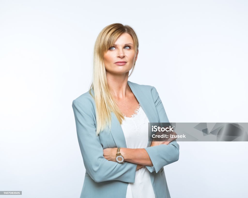 Portrait of confident businesswoman Portrait of confident mid adult woman standing with arms crossed and looking away. Studio shot, grey background. Blond Hair Stock Photo
